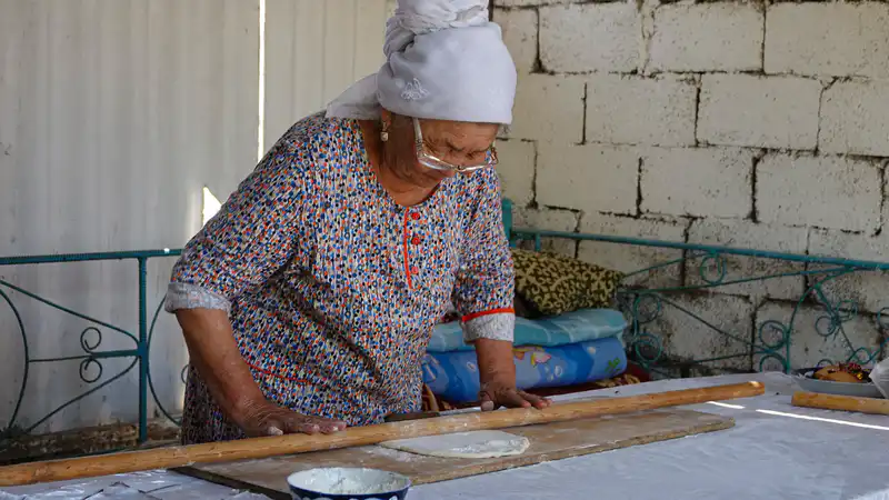 Пожилая женщина раскатывает тесто